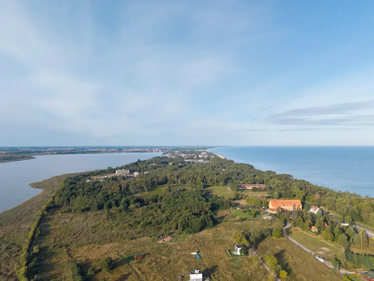 Widok z lotu ptaka na Mielno, gdzie jezioro Jamno styka się z Morzem Bałtyckim, otoczone lasem i zabudowaniami.