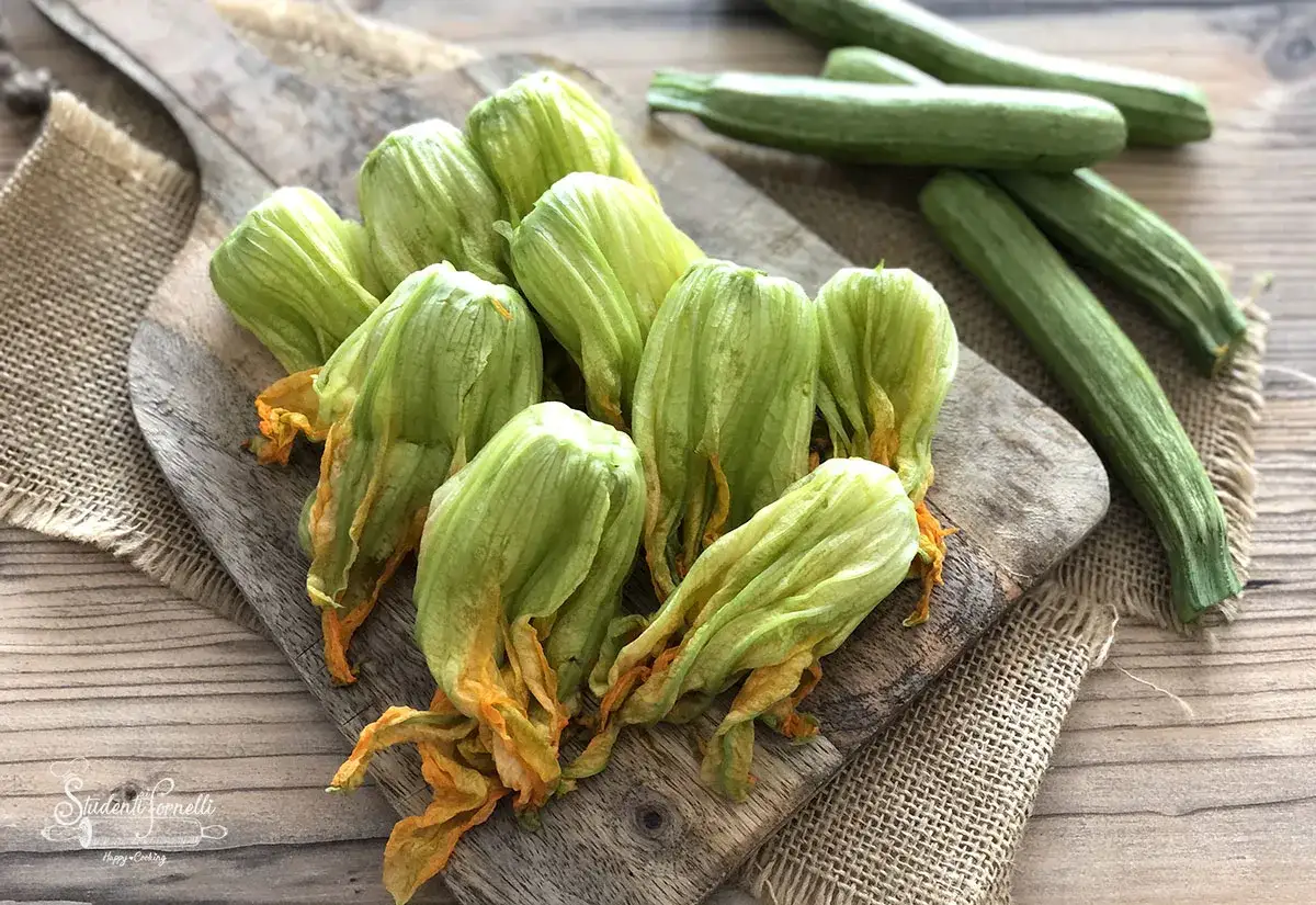 Fiori di zucca freschi pronti per deliziose ricette. Zucchine verdi sullo sfondo, ingredienti per un pasto estivo.