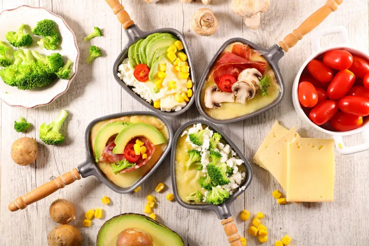 Quatre coupelles de raclette sans pomme de terre : avocat, maïs, brocolis, fromage blanc, tomates cerises, charcuterie et champignons.
