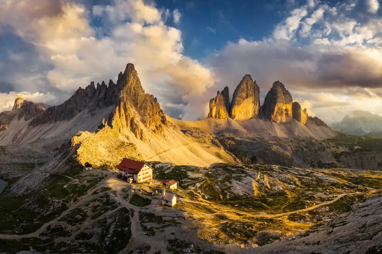 Góry Tre Cime di Lavaredo w Dolomitach skąpane w ciepłym świetle **golden hour**. Widoczne schronisko i malownicze szlaki.