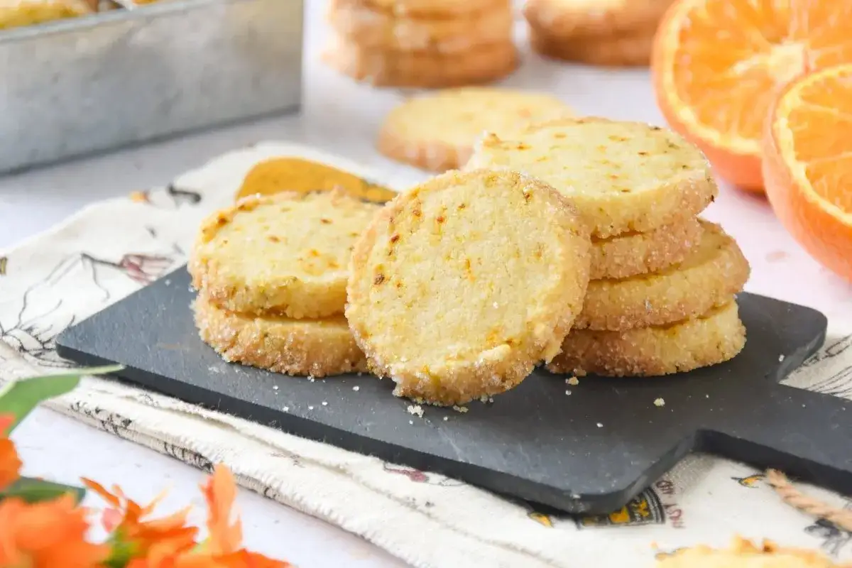 Deliciosas galletas de naranja, crujientes y con un toque cítrico, apiladas sobre una tabla negra.