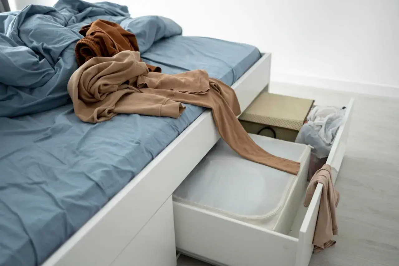 Cama con ropa encima y cajones abiertos mostrando ideas de almacenamiento de dormitorio con cajas y bolsas.