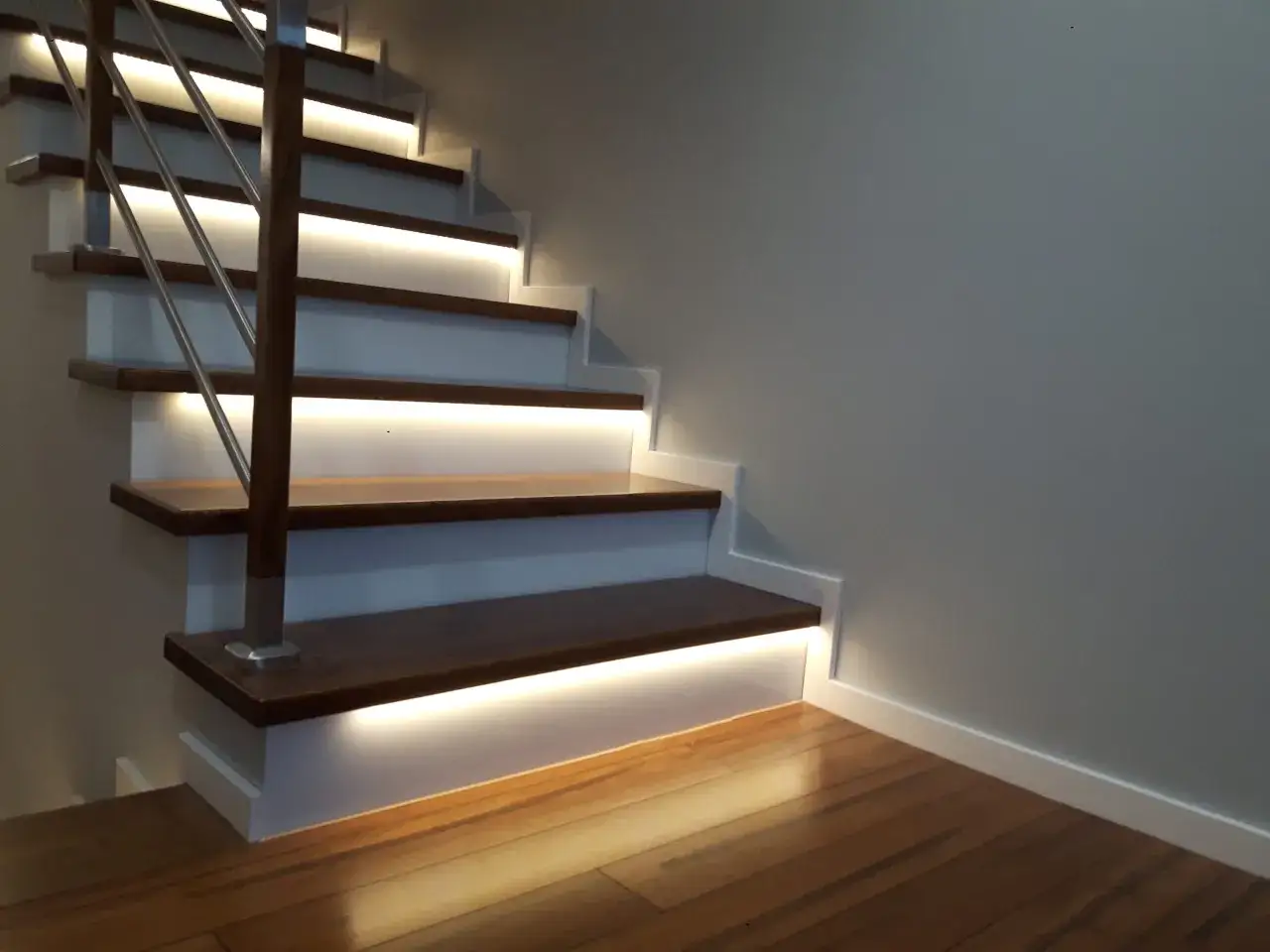 Nowoczesne schody drewniane wewnętrzne z podświetlanymi stopniami i metalową balustradą.