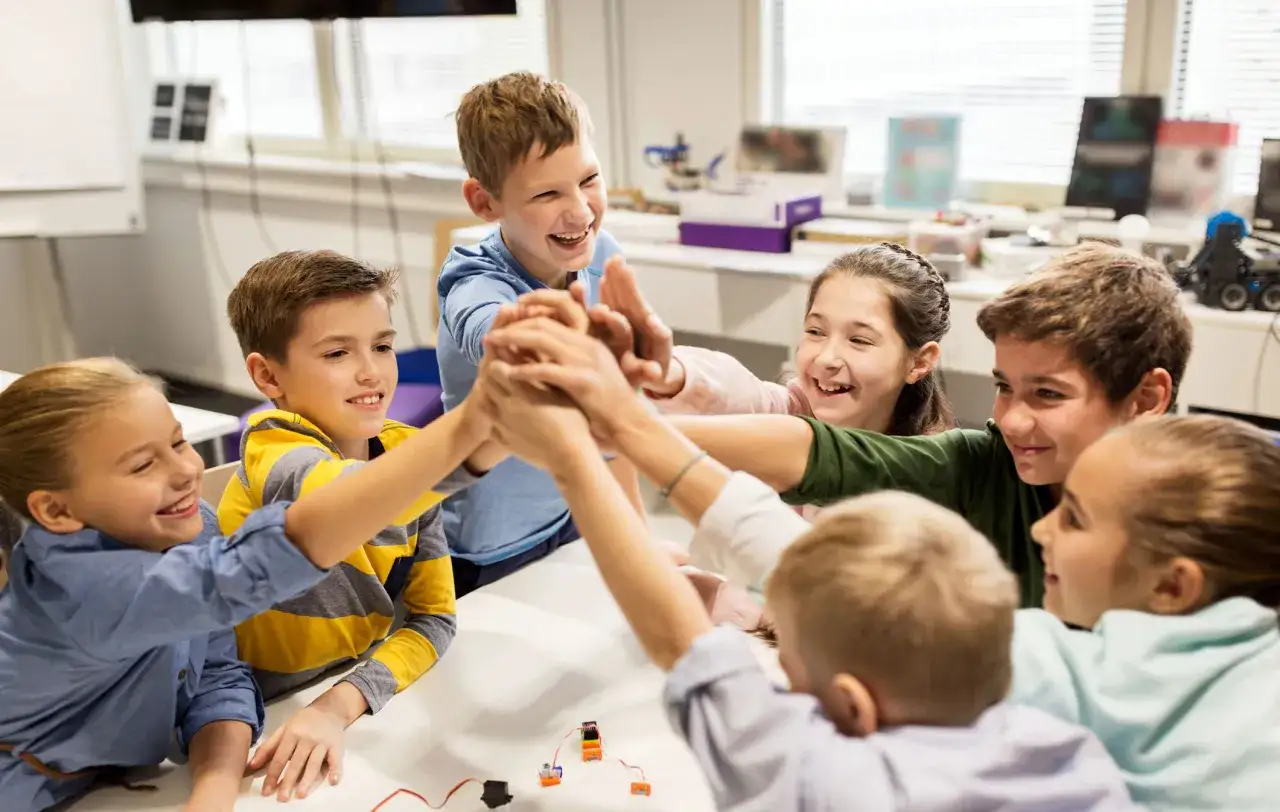 Kinder bilden eine Gruppe und legen ihre H&auml;nde &uuml;bereinander, um einen Erfolg zu feiern. Sie lachen und sind voller Energie.