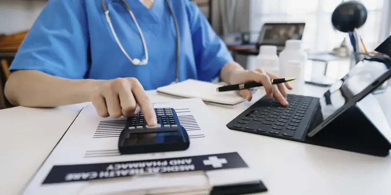 Profesional sanitario gestiona documentaci&oacute;n sanitaria online, usando calculadora y tablet.