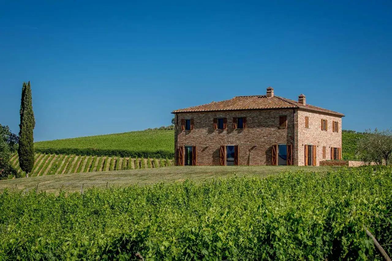 Azienda agricola Poliziano: casa in mattoni rossi tra rigogliosi vigneti sotto un cielo azzurro.