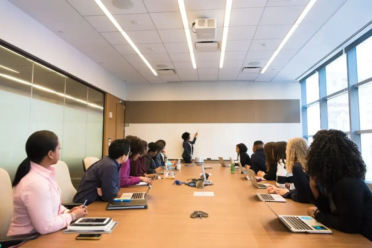 Gruppo di persone in riunione, una donna scrive su una lavagna. Dimostra che i master si possono fare senza laurea, puntando su competenze pratiche.