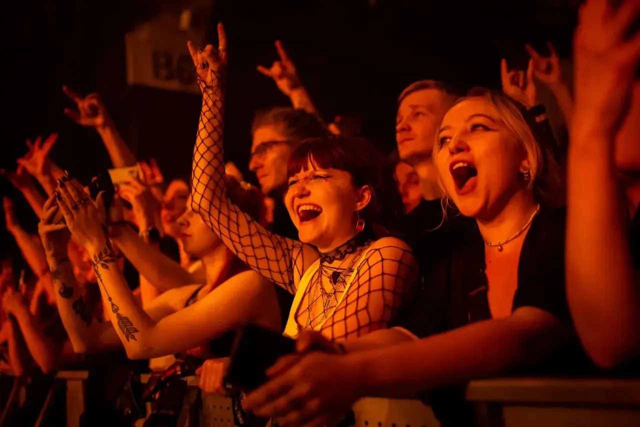 Fani na koncertach Three Days Grace krzyczą z radości, podnosząc ręce w geście rock'n'rolla.