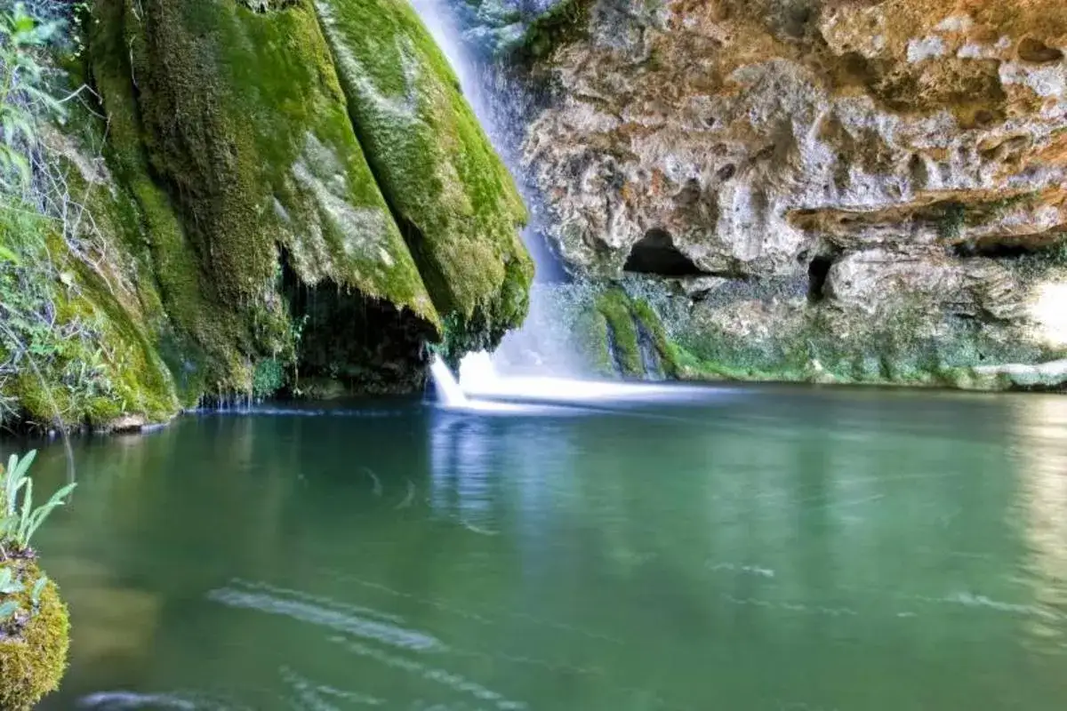 Cascada y poza de agua verde en un entorno rocoso y cubierto de musgo, un lugar id&iacute;lico para disfrutar de las piscinas naturales de Castell&oacute;n.