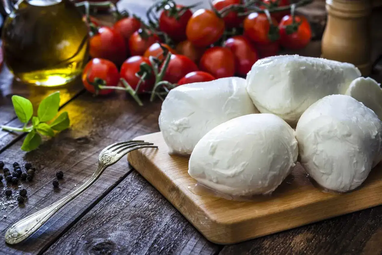 Świeża, włoska mozzarella na desce, obok pomidorków koktajlowych, oliwy i bazylii. Idealna na letnią sałatkę.