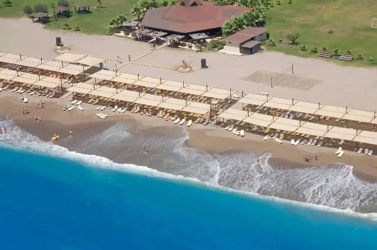 Słoneczna plaża z rzędami leżak&oacute;w i parasoli, w tle budynek restauracyjny. Idealne miejsce na wakacje w Serra Palace, Turcja.
