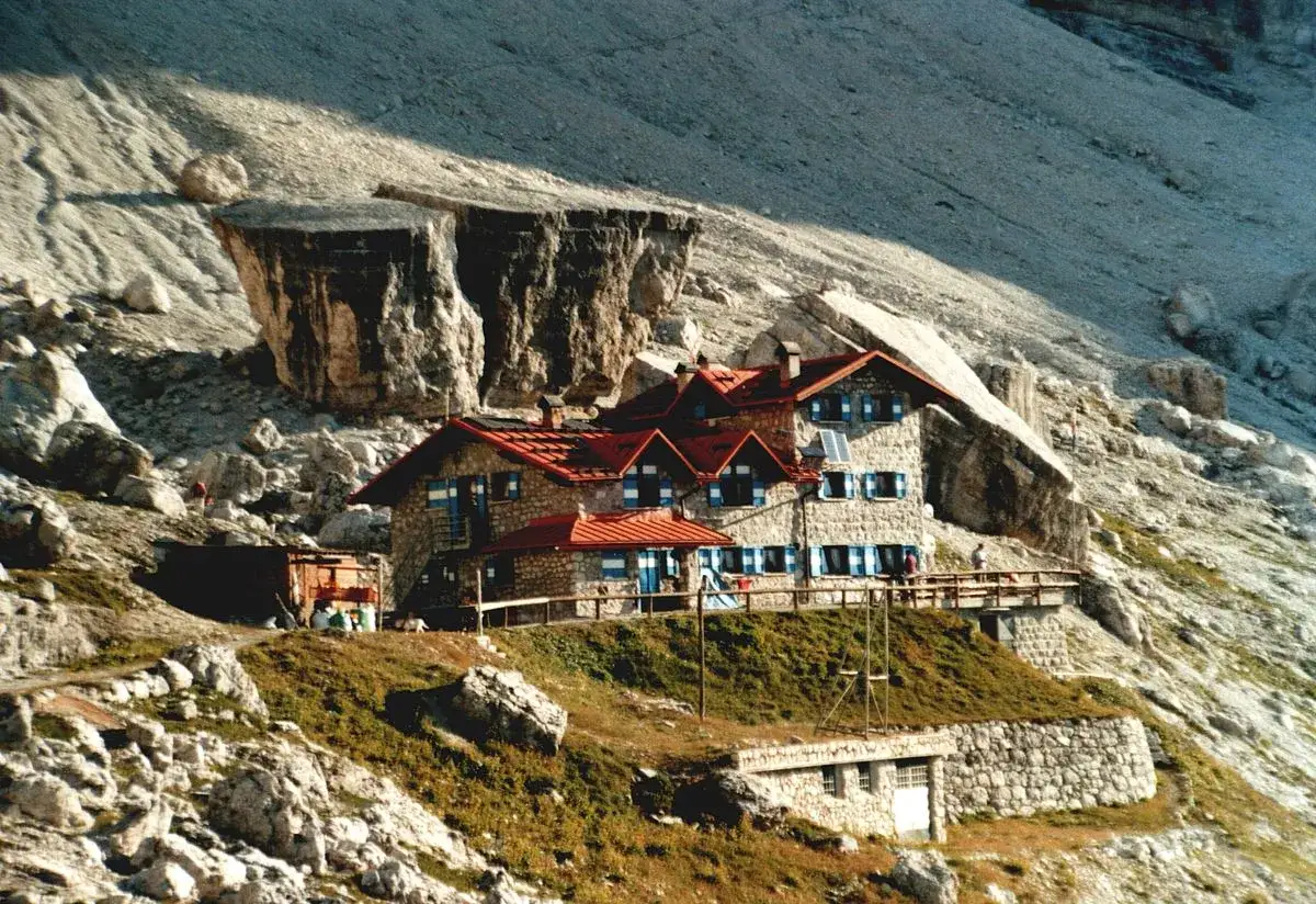 Rifugi alto Adige in pietra, con tetti rossi, incastonati tra rocce imponenti e pendii erbosi.