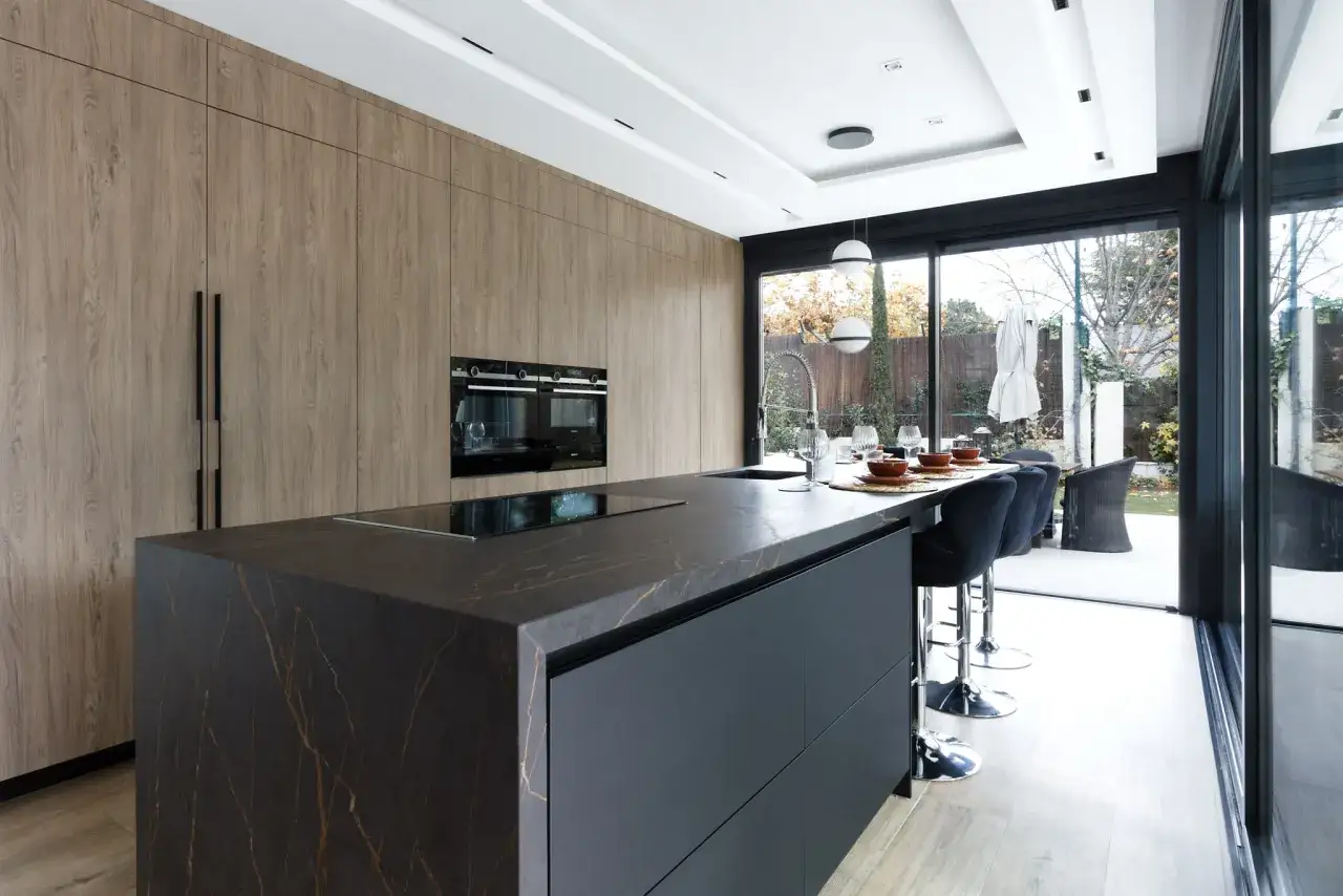 Elegantes cocinas en negro con isla de cuarzo veteado, gabinetes de madera y electrodomésticos integrados.