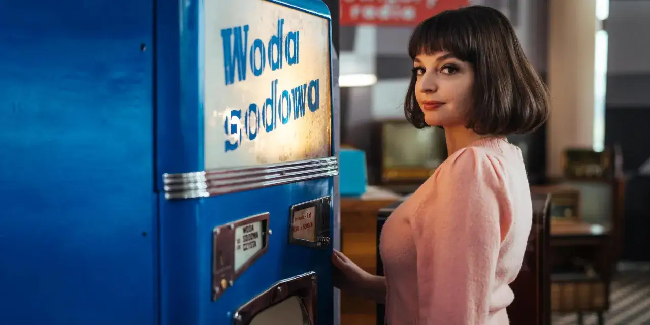 Maria Dębska w różowym sweterku przy saturatorze. Scena jak z filmów z lat 80.