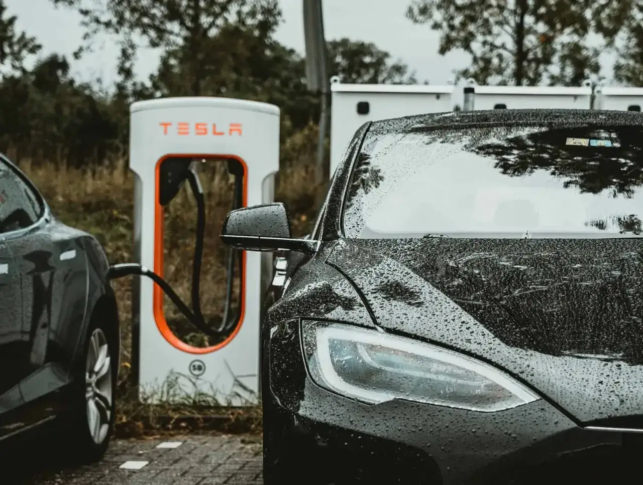 Czarna Tesla na deszczu ładuje się przy stacji Supercharger. Czas ładowania zależy od modelu i stanu baterii.