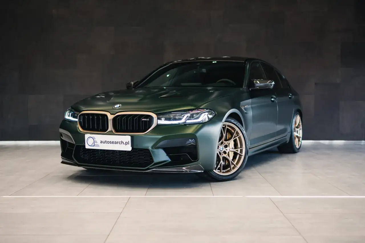 Mocny BMW M5 CS w kolorze ciemnozielonym z brązowymi felgami, gotowy do jazdy.