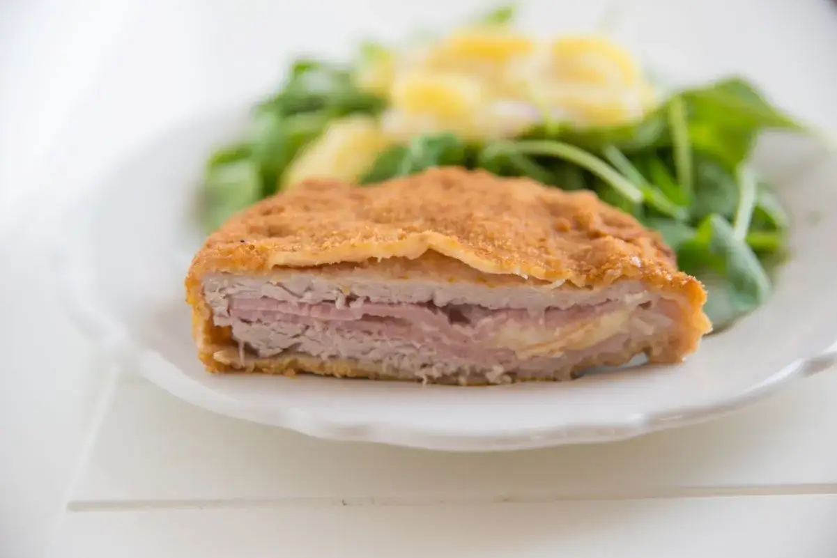 Kotlet po szwajcarsku, panierowany, z szynką i serem, podany z sałatką.