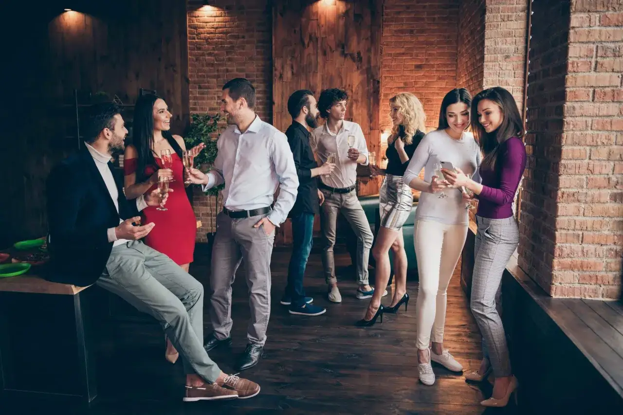 Grupo de personas en una fiesta, cumpliendo el codigo de vestimenta formal. Conversan y brindan con copas de champán.