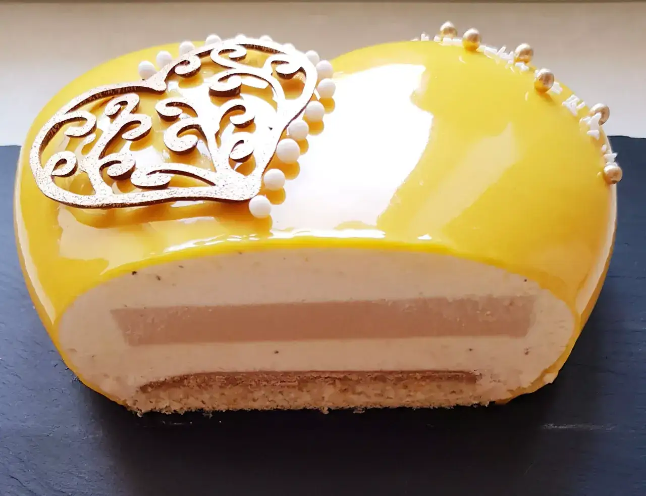 Gâteau cœur jaune brillant, glaçage miroir, décoré de perles et d'une arabesque dorée. L'intérieur révèle des couches crémeuses et une touche de caramel facile.