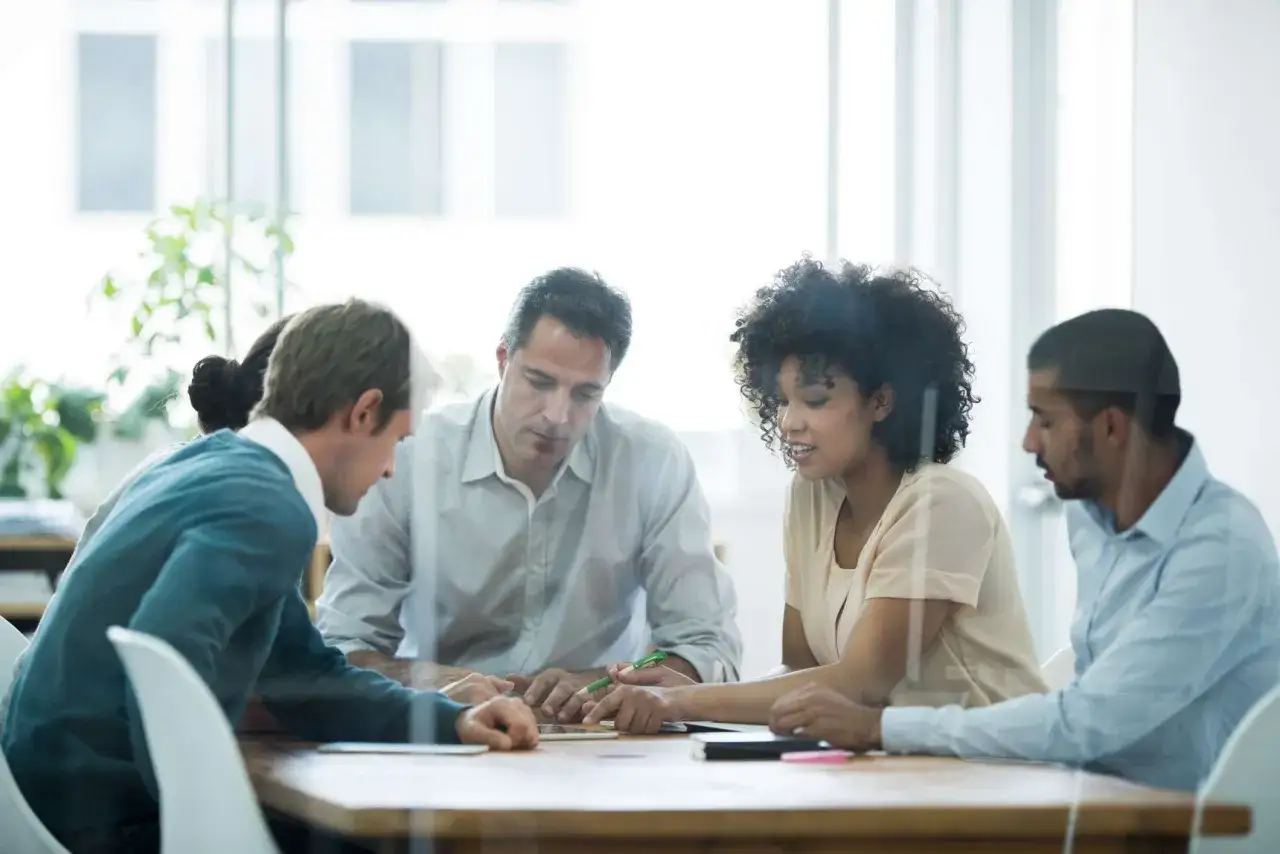 Un gruppo discute animatamente, forse per evitare il groupthink cos'&egrave;. Si scambiano idee attorno a un tavolo.
