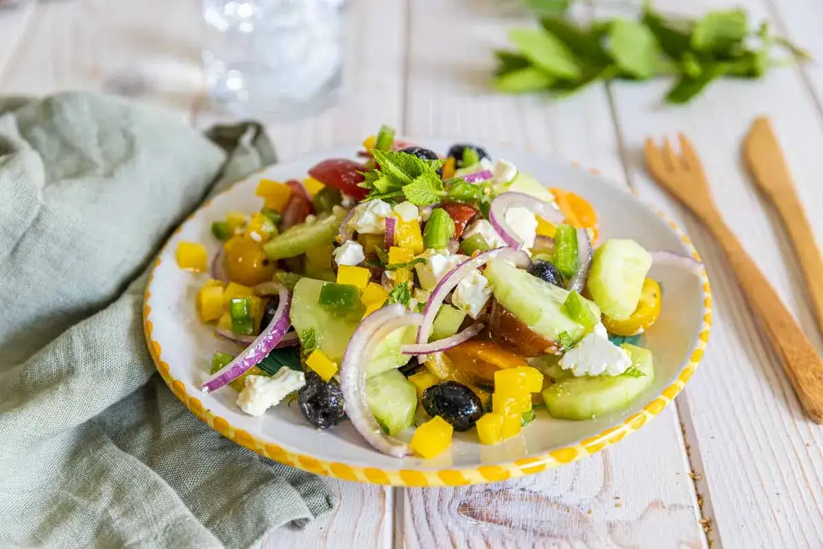 Une assiette colorée de salade à la grecque, garnie de feta, olives, concombres, tomates et poivrons, prête à être dégustée.