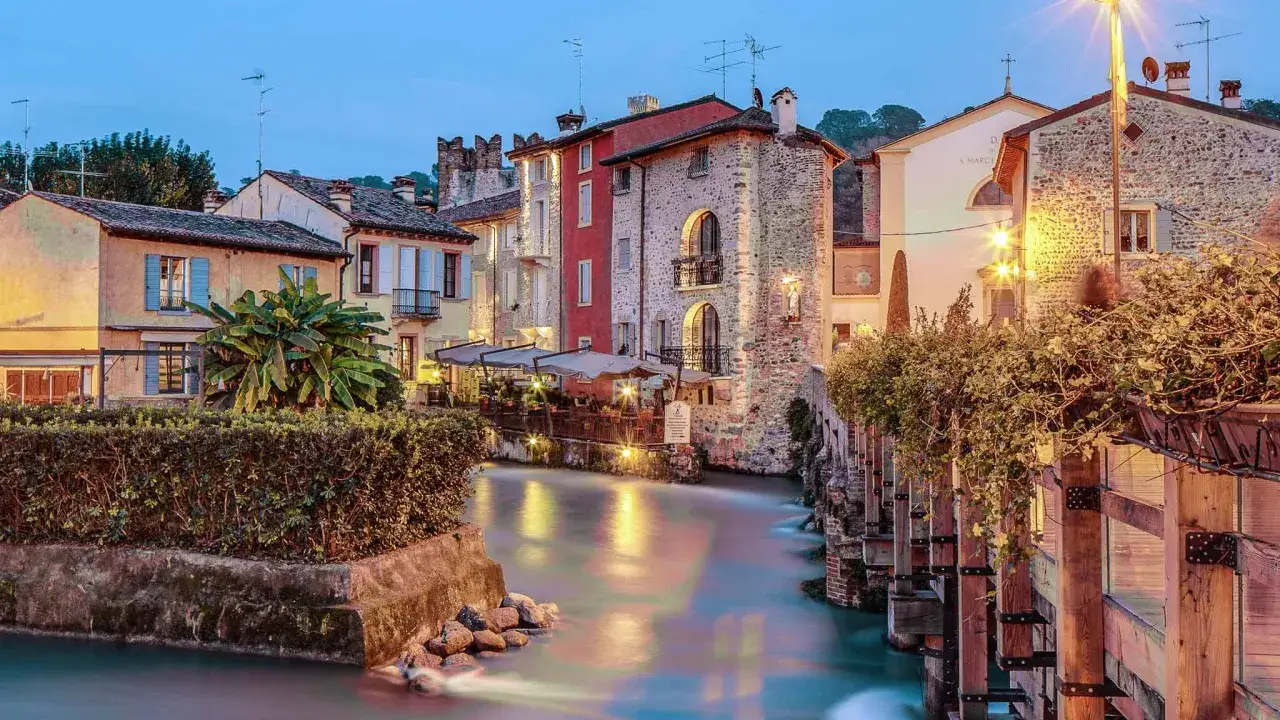 Un incantevole borghetto a Mantova, con case colorate affacciate su un canale illuminato, crea un'atmosfera magica al crepuscolo.