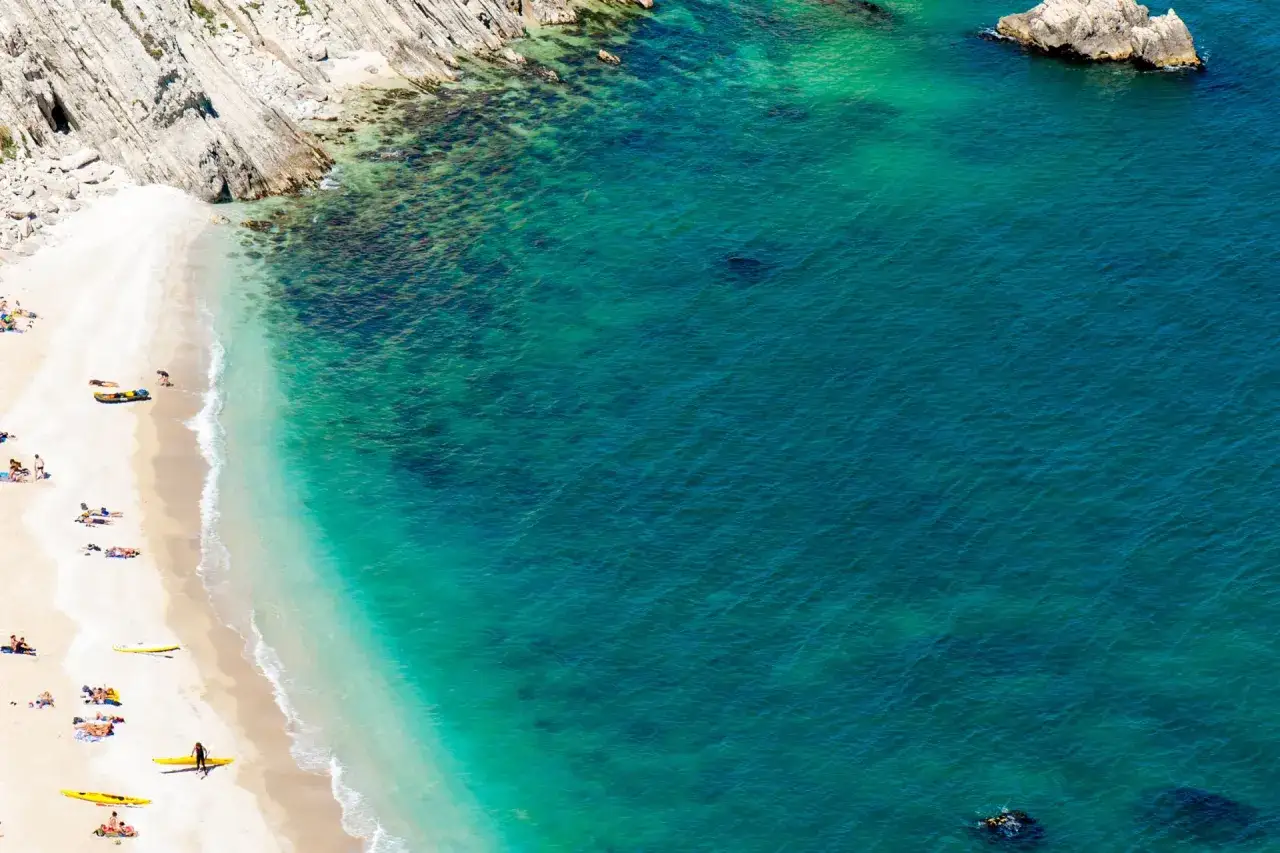 Spiaggia dorata e acqua cristallina, un sogno di vacanza a Riccione. Il mare turchese invita a tuffarsi, mentre bagnanti e kayak godono del sole.