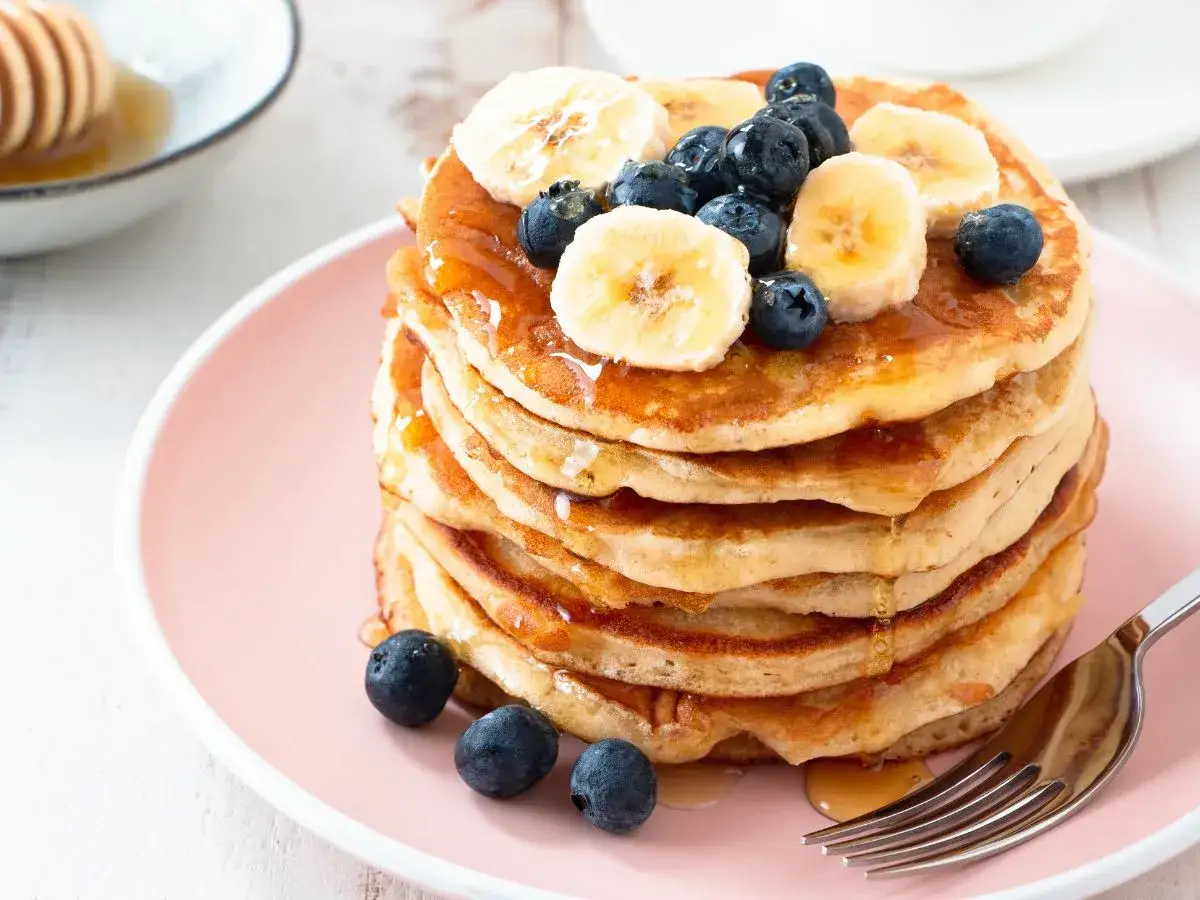 Pyszny stos pancake'ów z bananem i borówkami, polany syropem. Idealny przepis na śniadanie.