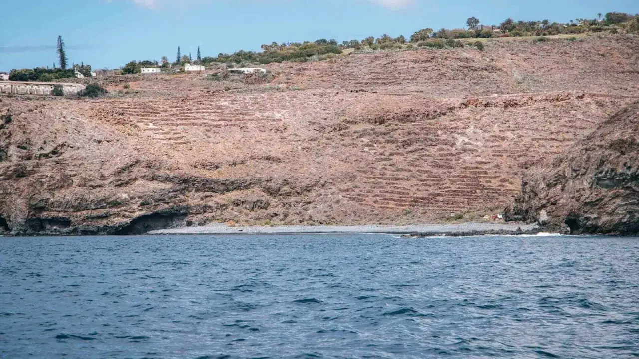 Vista desde el mar de la playa del medio, con acantilados rocosos y terrazas de cultivo en la ladera.