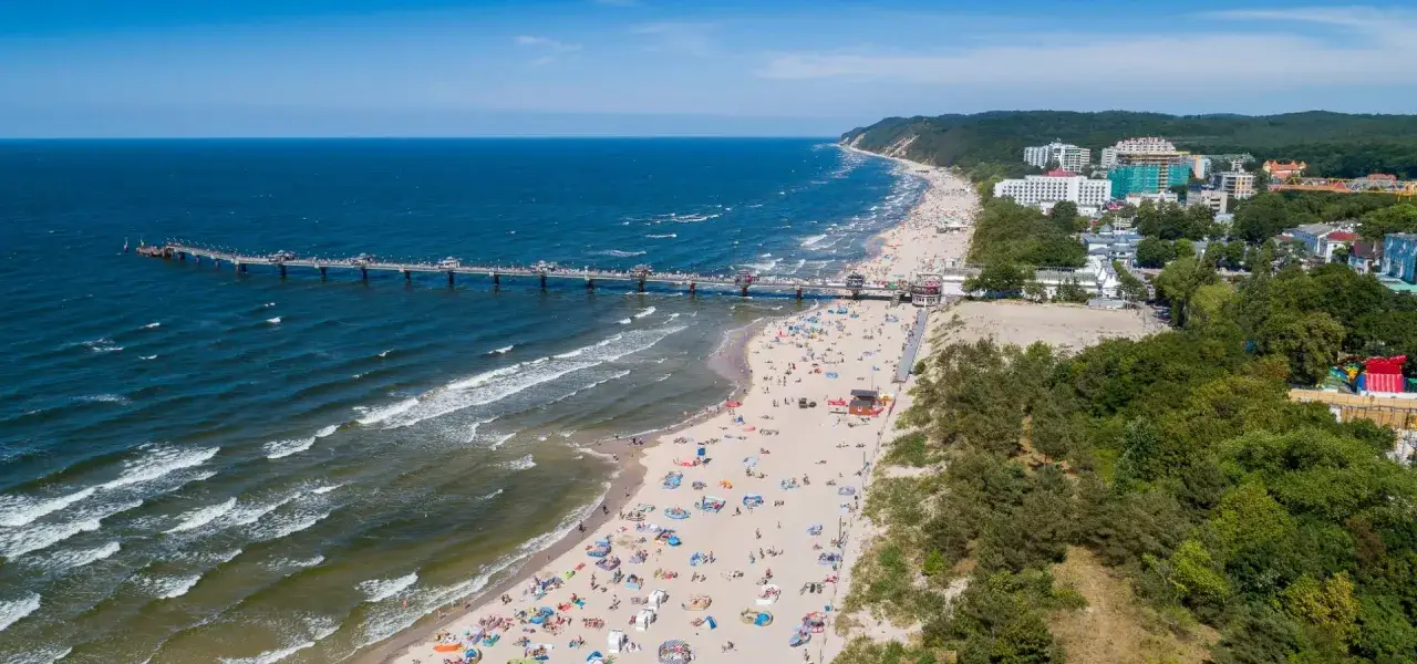 Słoneczna plaża w Międzyzdrojach z molo i tłumem turystów. Wspaniałe międzyzdroje atrakcje oferują relaks nad morzem.