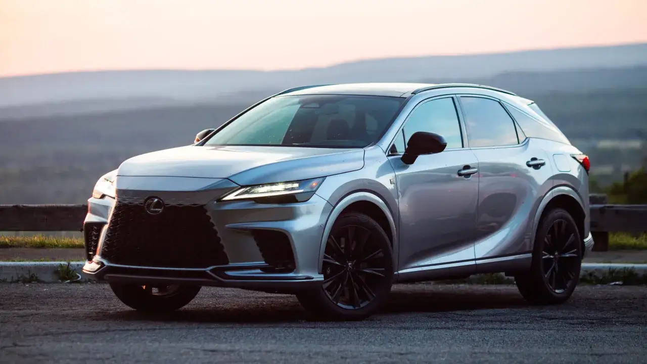Srebrny Lexus RX500h z czarnymi felgami na tle zachodzącego słońca i górskiego krajobrazu.