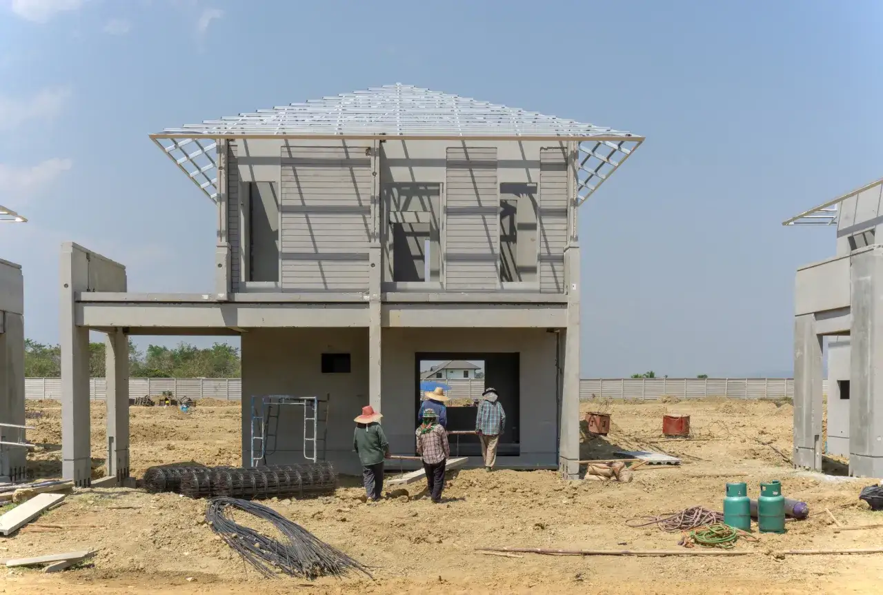 Budowa domu prefabrykowanego betonowego. Trzech robotników w kapeluszach idzie w kierunku otwartego wejścia.
