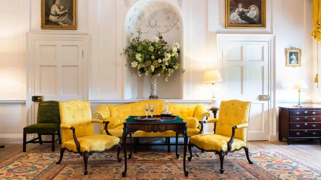Elegancki salon z żółtą kanapą i fotelami w stylu **chippendale**, ozdobiony bukietem kwiatów i obrazami.