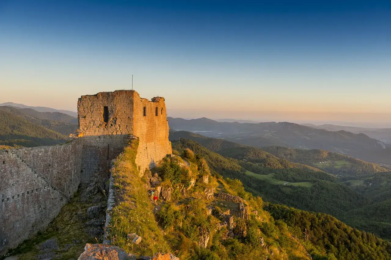 Ruines d'un château cathare baignées par le soleil couchant, sur le sentier cathare GR 367. Paysage de montagnes verdoyantes.