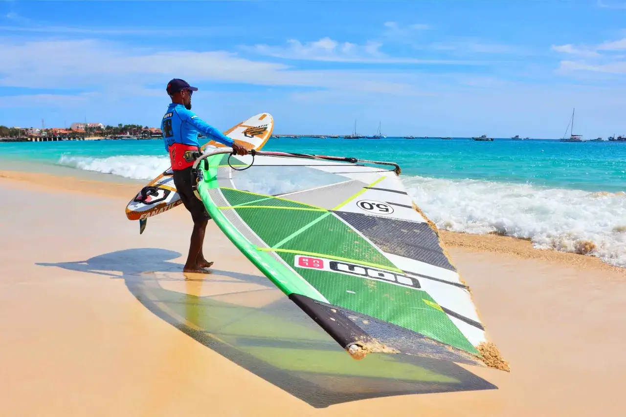 Mann mit Windsurf-Ausrüstung am Strand der Kapverden, bereit für das Windsurfen Kapverden.