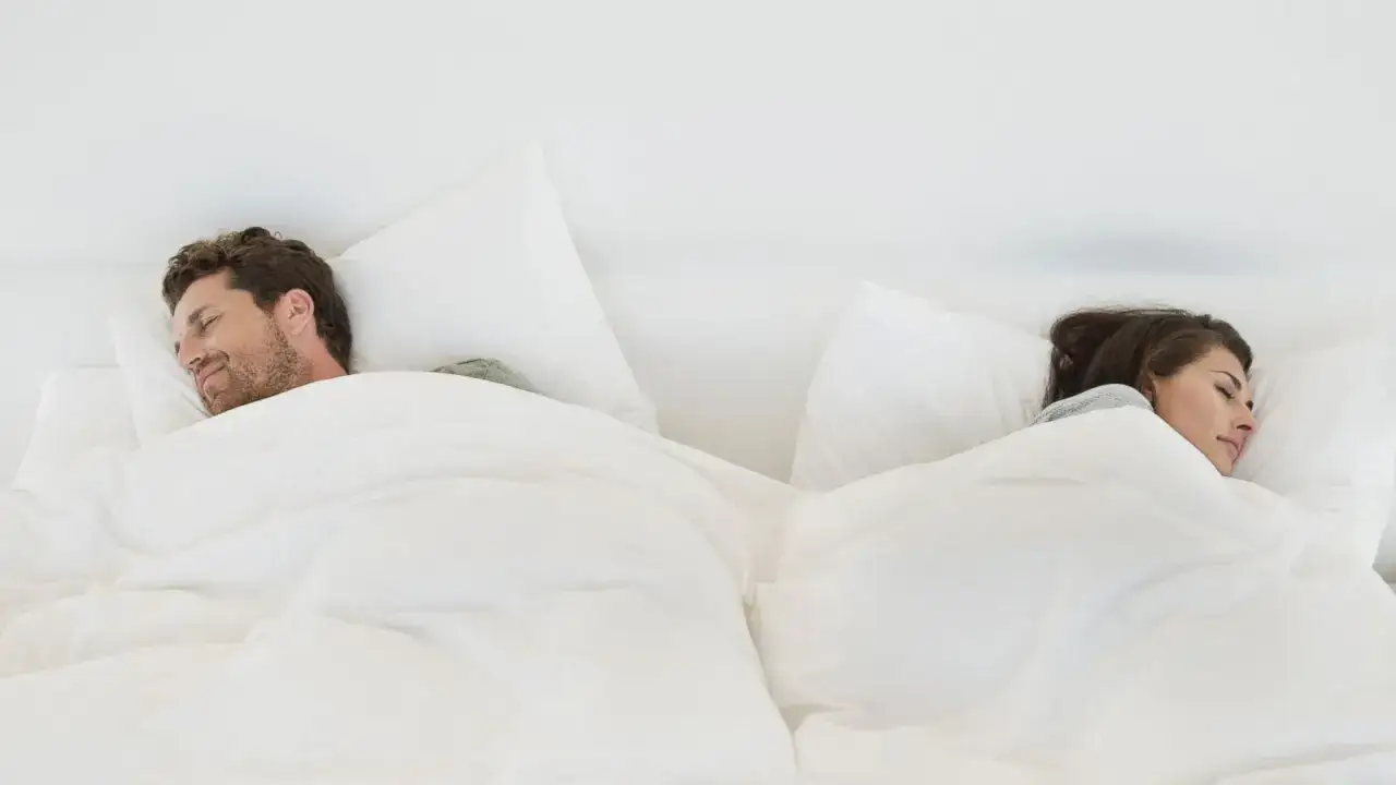 A couple sleeps separately in a large bed, a visual metaphor for sleep divorce.