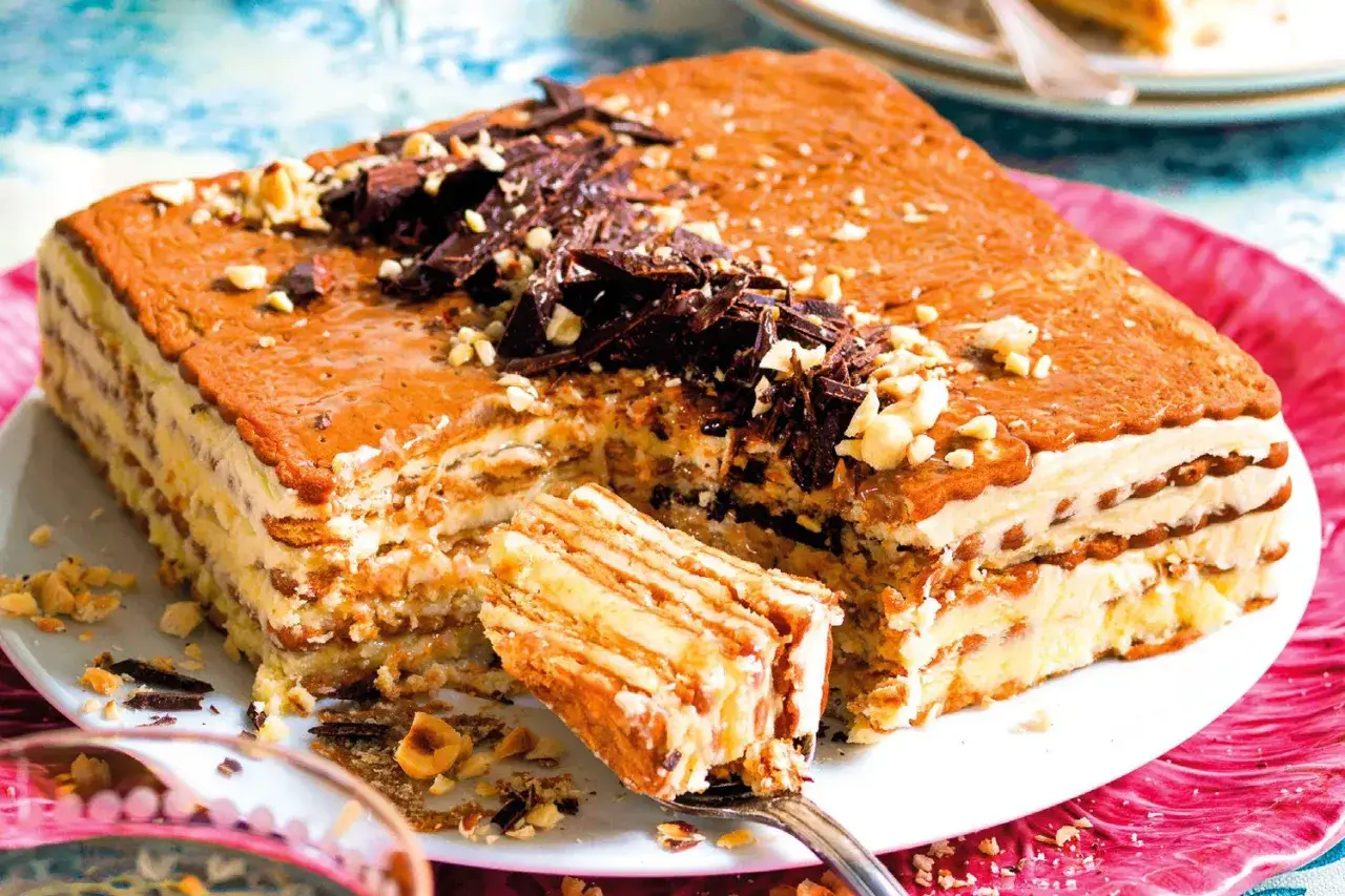 Torta fredda a strati con biscotti, crema al burro e scaglie di cioccolato. Una fetta è già stata prelevata con una forchetta.
