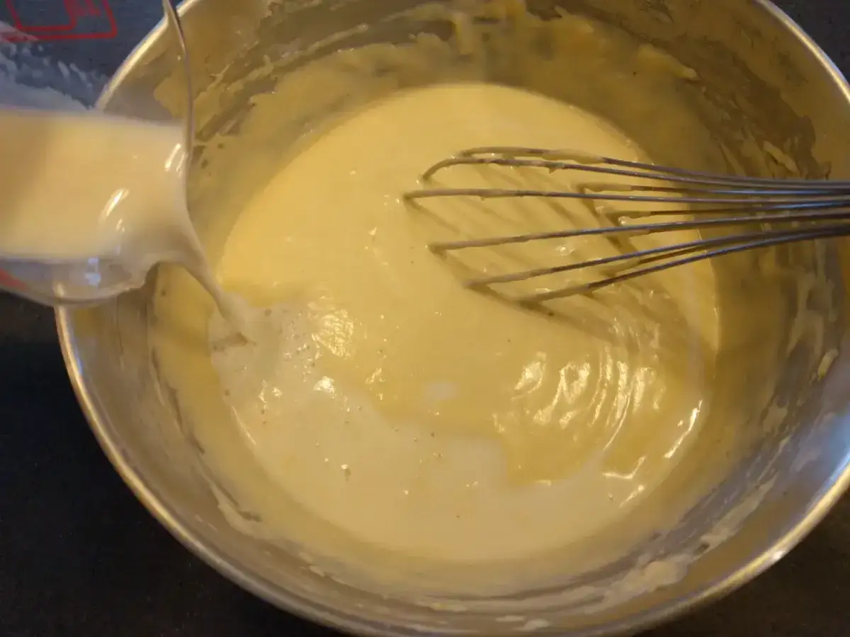 Verser du lait dans une pâte à gaufre épaisse dans un bol avec un fouet.