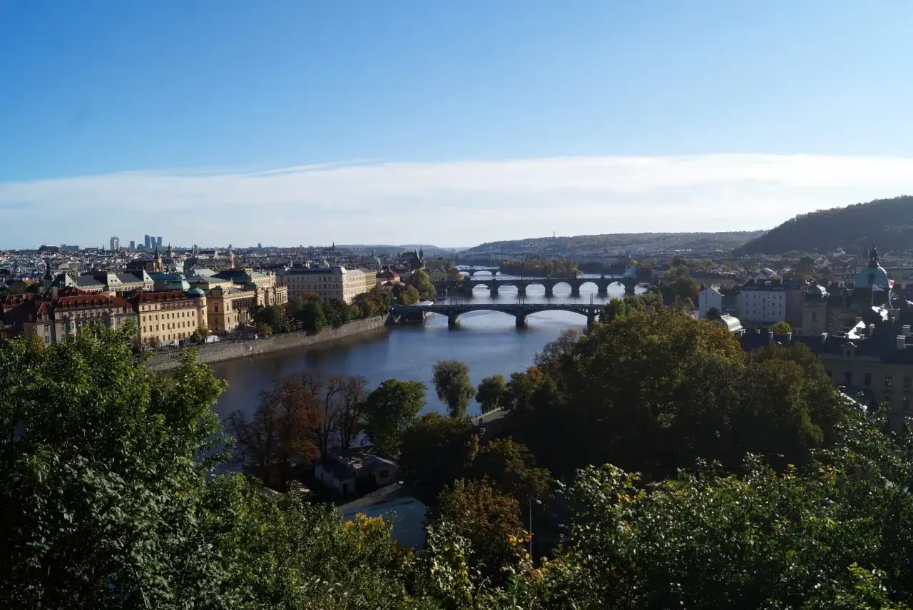 Vue panoramique de Prague en ce moment, avec le fleuve Vltava travers&eacute; par plusieurs ponts, des b&acirc;timents historiques et des collines verdoyantes.