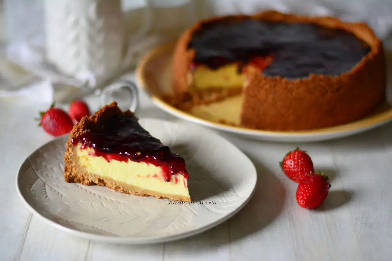 Una fetta di cheesecake cotta, con una crosta dorata e un ripieno cremoso, guarnita con confettura di frutti rossi e fragole fresche.