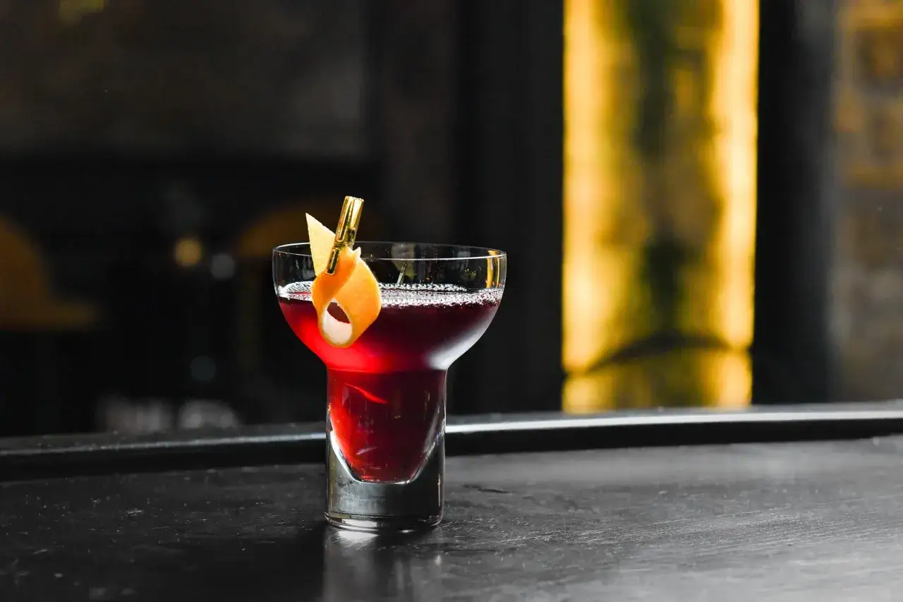 Eleganckie drinki z whisky, jeden z nich ozdobiony skórką pomarańczy, na ciemnym blacie.