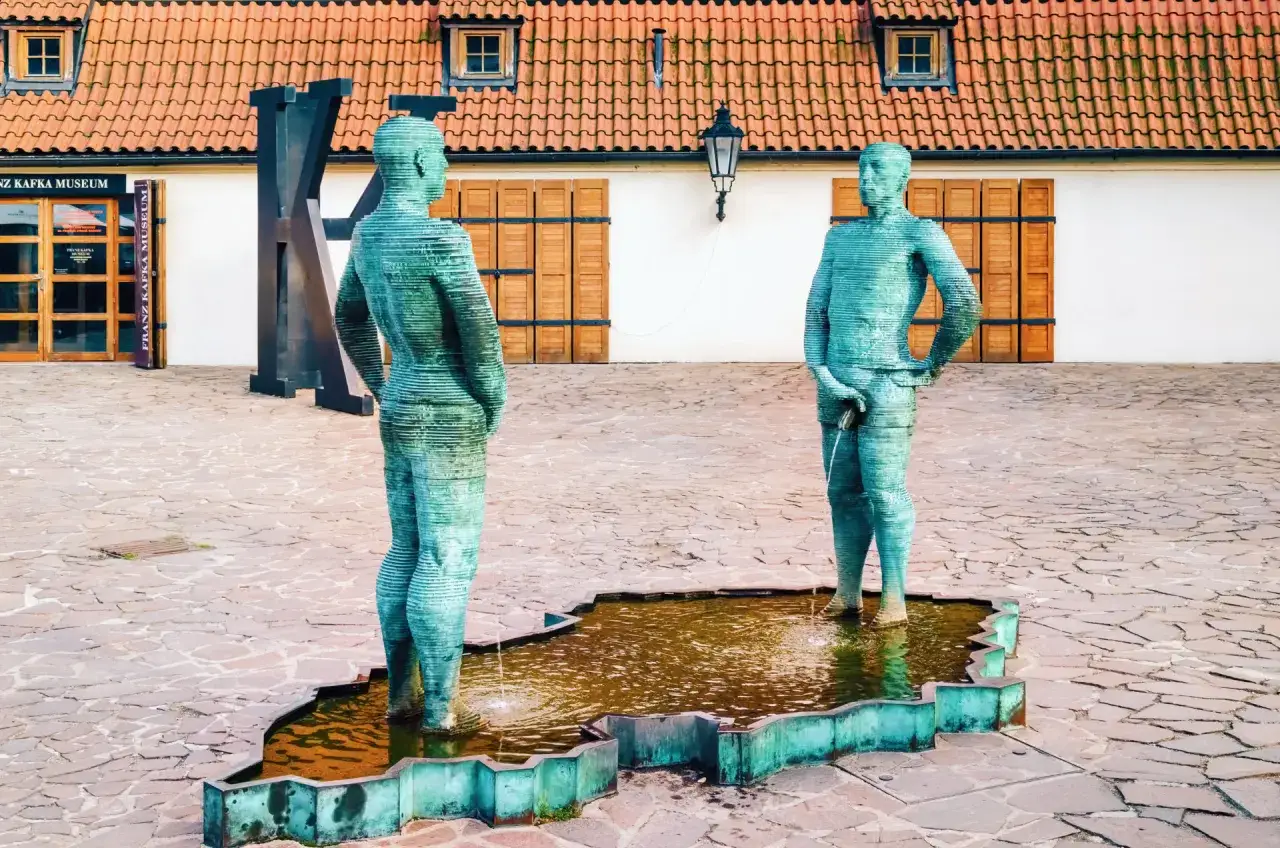 Fontanna z rzeźbami w kształcie ludzi, przed Muzeum Franza Kafki. Ciekawe, czy pisarz też by się uśmiechnął, widząc te **franz kafka ciekawostki**?