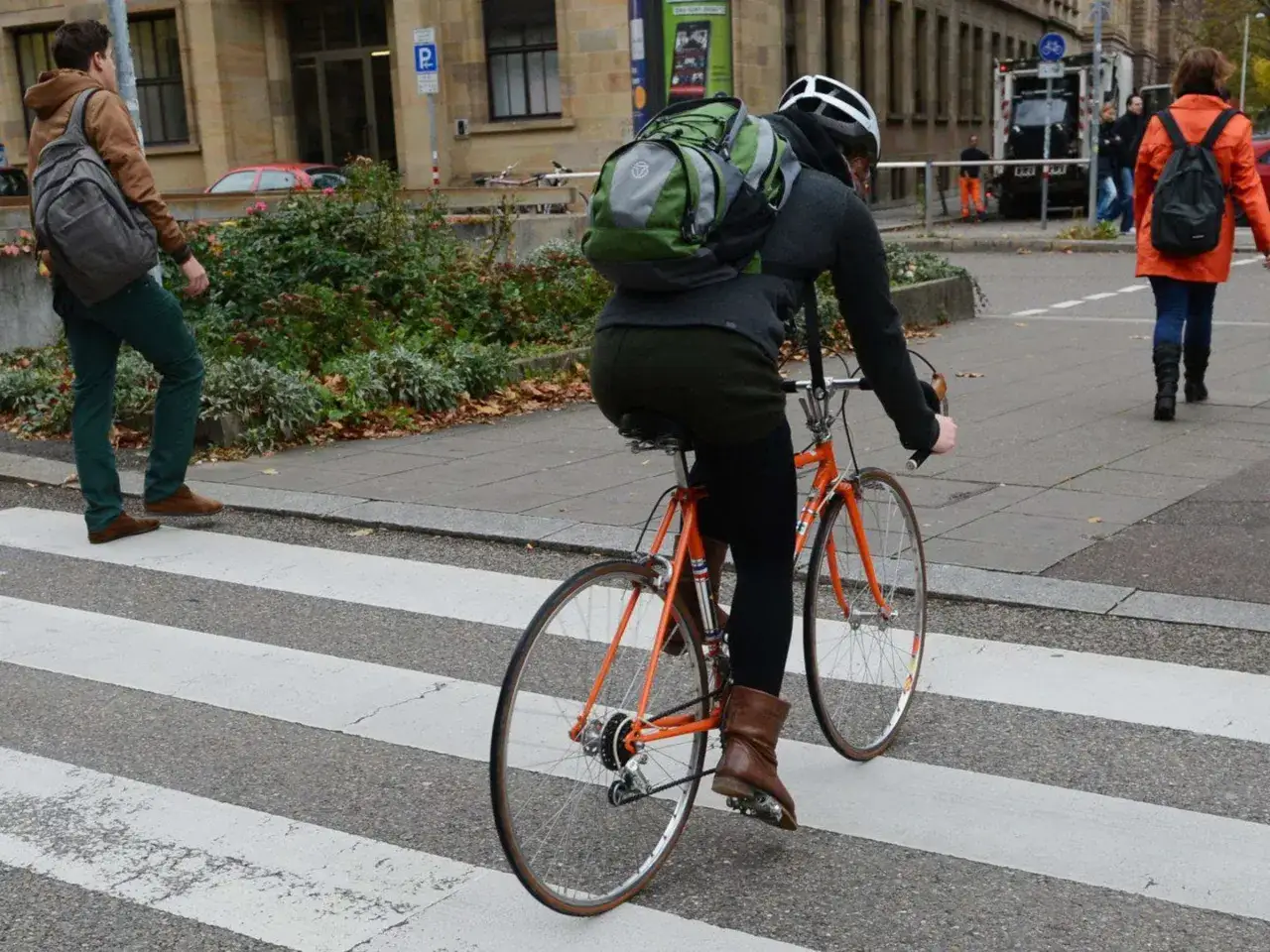 Fahrradfahrer mit Rucksack &uuml;berquert den Zebrastreifen.