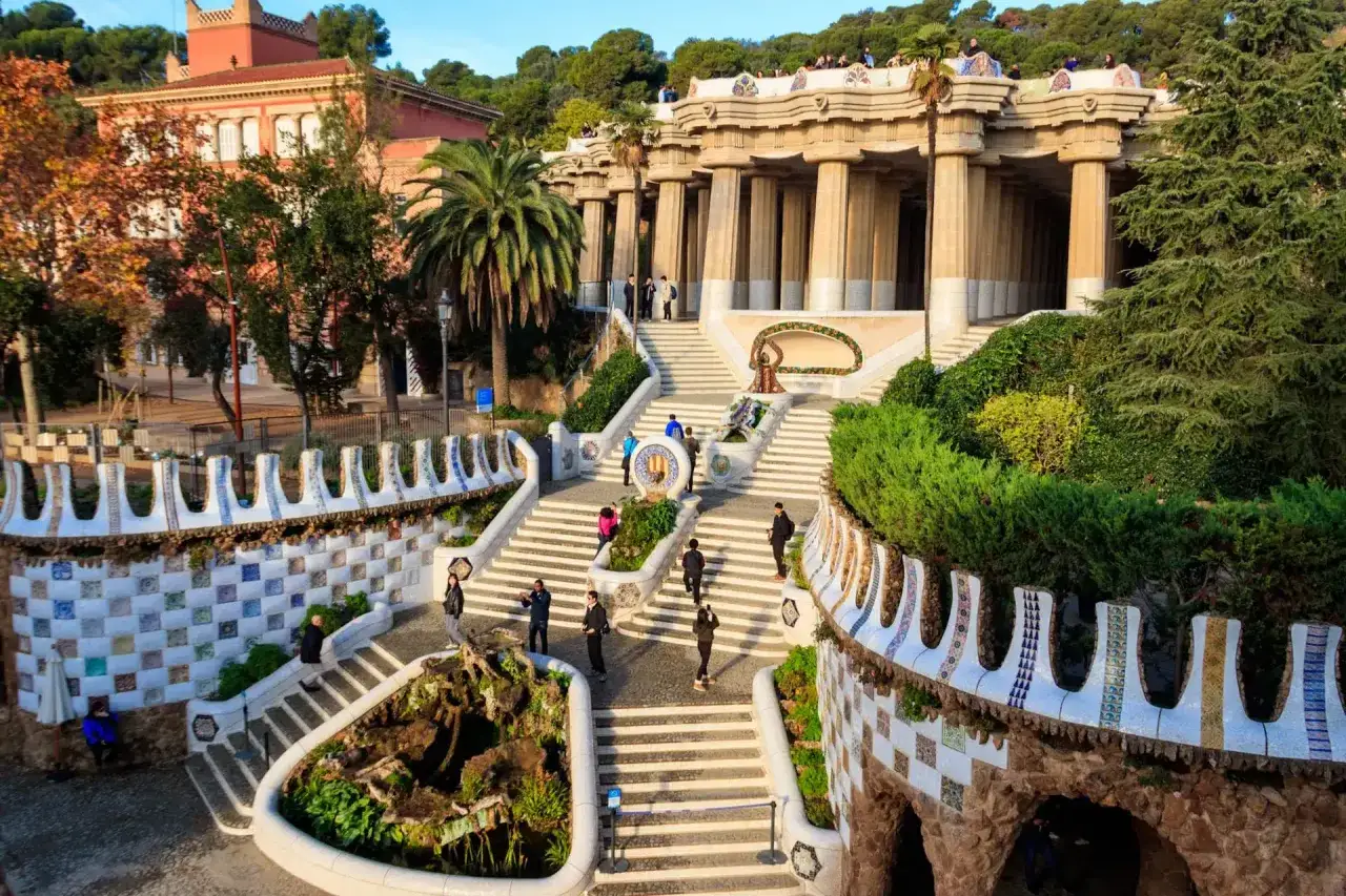 Kolorowe mozaiki i kolumnowy pawilon w Parku G&uuml;ell. Ludzie spacerują po schodach, podziwiając architekturę.
