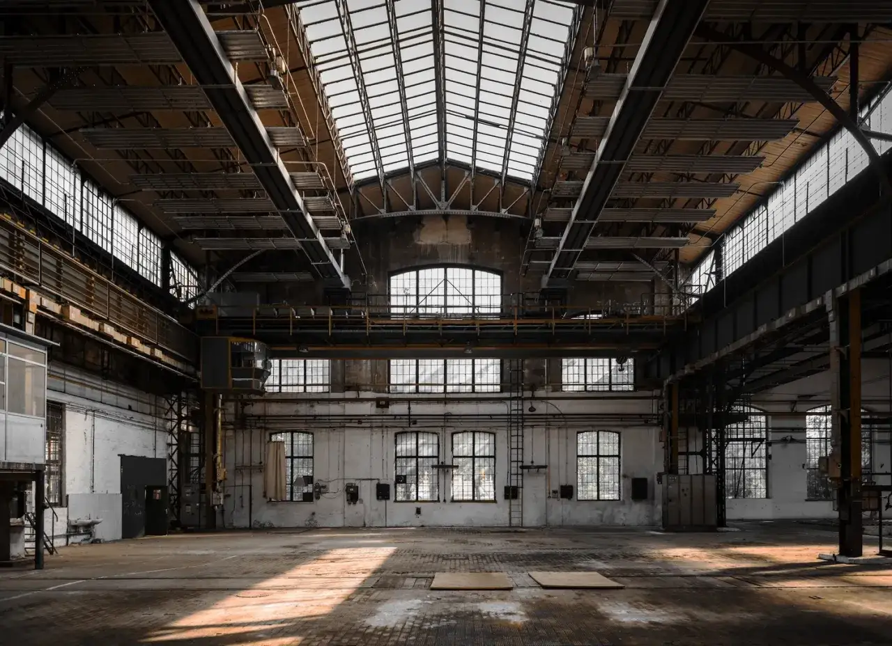 Große, leere Industriehalle mit Oberlichtern und Kranbahn. Ein Symbol für den **regionalen Strukturwandel** und die Transformation von Industrielandschaften.