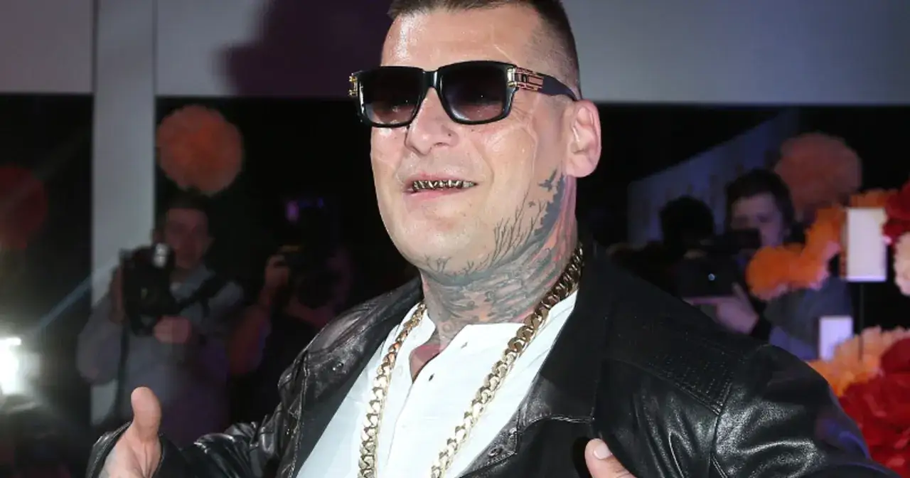 Popek kiedys, w okularach i z złotymi zębami, pozuje z łańcuchem na szyi.