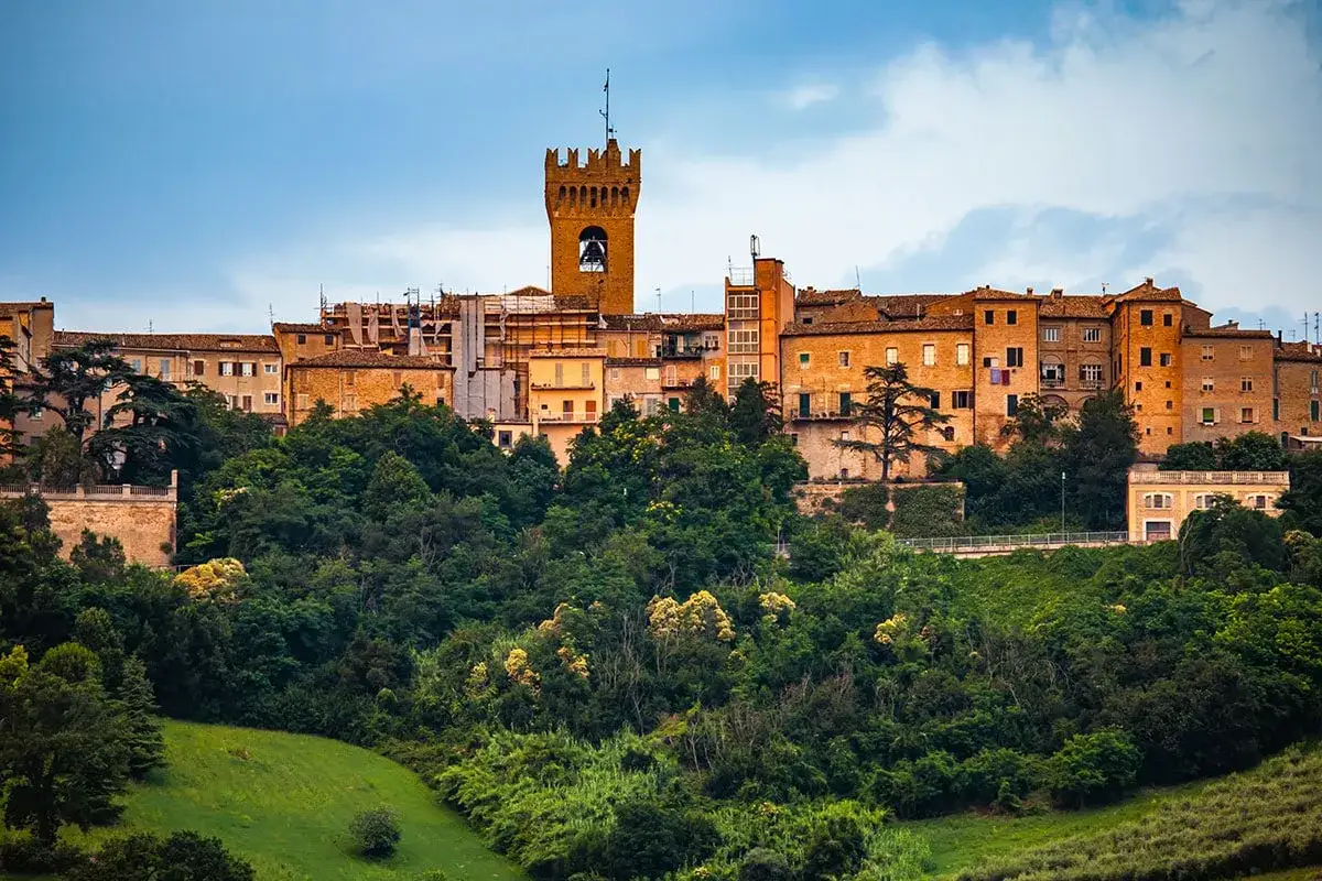 Antica città di Leopardi, arroccata su una collina verdeggiante, con un campanile che domina il paesaggio.