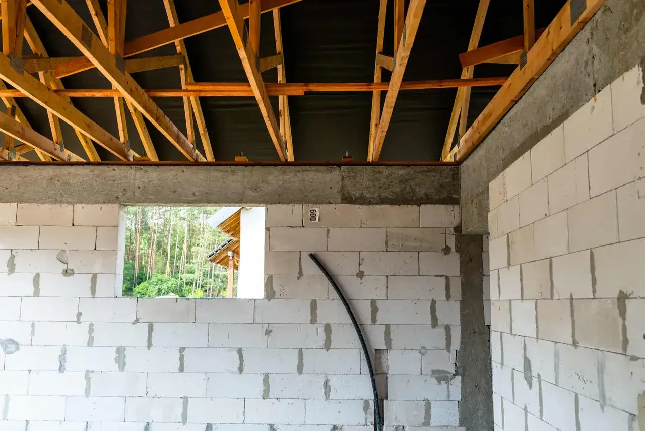 Budowa domu w toku. Widoczny betonowy wieniec stropowy, ściany z bloczków gazobetonowych i drewniana konstrukcja dachu.