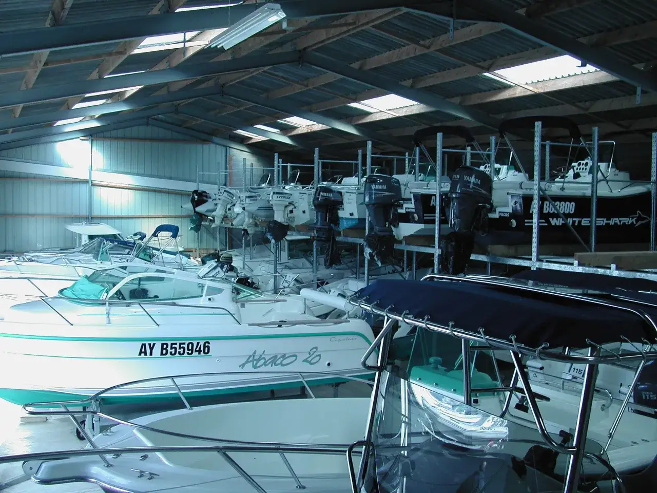 Plusieurs bateaux &agrave; moteur sont rang&eacute;s sur des &eacute;tag&egrave;res dans un entrep&ocirc;t, pr&ecirc;ts pour la saison. Le cale bateau est bien rempli.