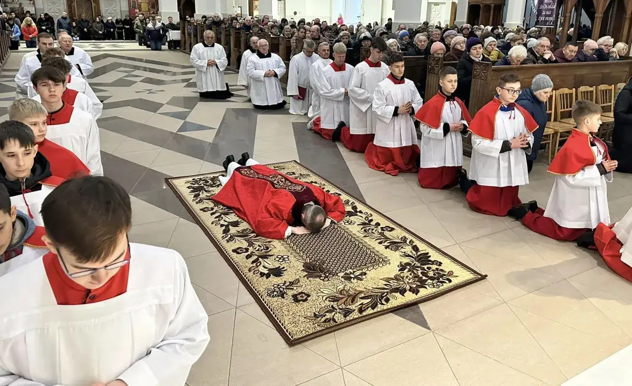 Podczas liturgii Męki Pańskiej klęczący wierni i ministranci w kościele. Kapłan leży krzyżem na dywanie.